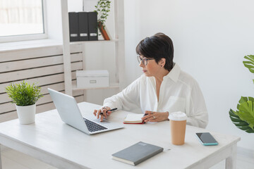 Middle-aged beautiful woman smiling while working with laptop in office - business and manager works concept