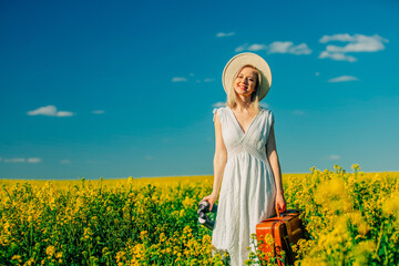 Fototapeta premium Beautiful woman in dress with suitcase in rapeseed field