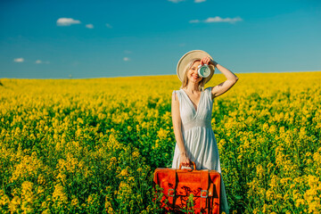 woman in dress with suitcase and alarm clock in rapeseed field