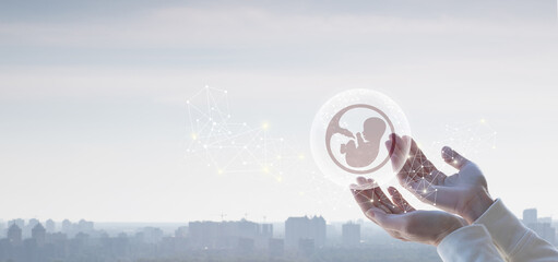 Hands support the human embryo on the background of the city .