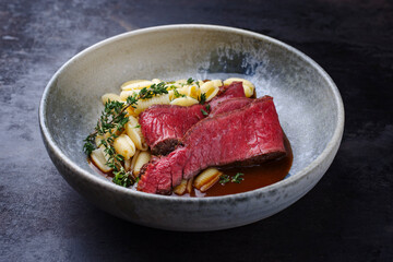 Traditional Italian chianina sliced roast beef with gnocchetti sardi pasta in spicy red wine sauce served as close-up in a Nordic design bowl with copy space