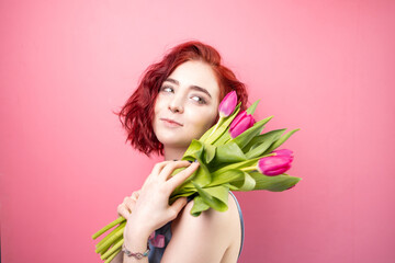 Obraz na płótnie Canvas Portrait of a beautiful young red head girl holding a bouquet of irises and tulips isolated on a pink background