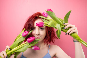 Portrait of a beautiful young red head girl holding a bouquet of irises and tulips isolated on a pink background