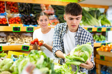 Positive couple standing together in fruit and vegetable section of supermarket and choosing ripe vegetables