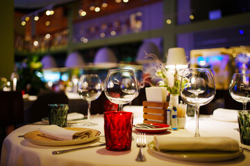 a table with a white tablecloth, glasses, crockery and decor in dark restaurant