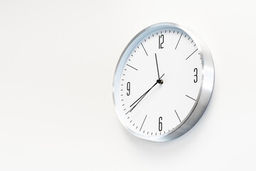 Stylish, round, white clock hangs on a white wall. Place for text, copy space.