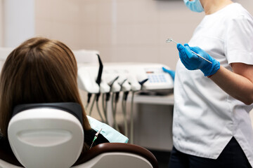 Obraz premium Female patient sitting in the dental chair, the dentist is holding a dental mirror in his hand, he will examine the patient's teeth. Professional dental treatment.