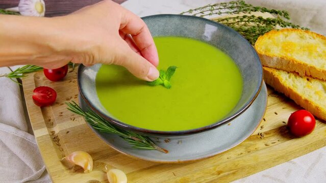 Person Serving Green Cream Vegetable Soup In Bowl, Adding Mint Leaf, Healthy Eating, Spinach Puree Soup, 4k Video, Slow Motion Footage