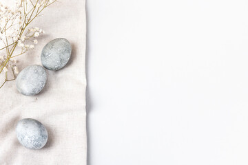 Grey Easter eggs with a sprigs of gypsophila on a linen towel on a grey background. Minimalism, copy space, flat lay