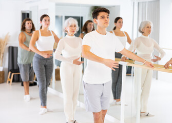 Fototapeta premium Group of dancers doing exercises using ballet barre in a modern fitness studio.