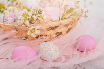 Easter candy chocolate eggs and almond sweets lying in a bird's nest decorated with flowers and feathers on white wooden background. Happy Easter concept.