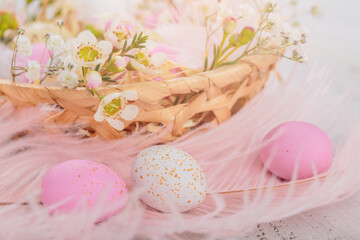 Obraz na płótnie Canvas Easter candy chocolate eggs and almond sweets lying in a bird's nest decorated with flowers and feathers on white wooden background. Happy Easter concept.