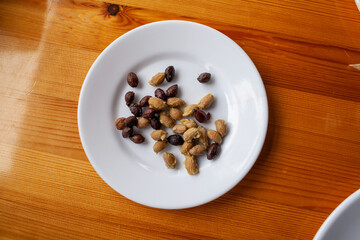 A plate of olive (Olea europaea) seeds on a white plate with wooden background. Green and black olive seeds 