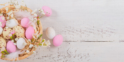 Fototapeta na wymiar Easter candy chocolate eggs and almond sweets lying in a bird's nest decorated with flowers and feathers on white wooden background. Happy Easter concept.