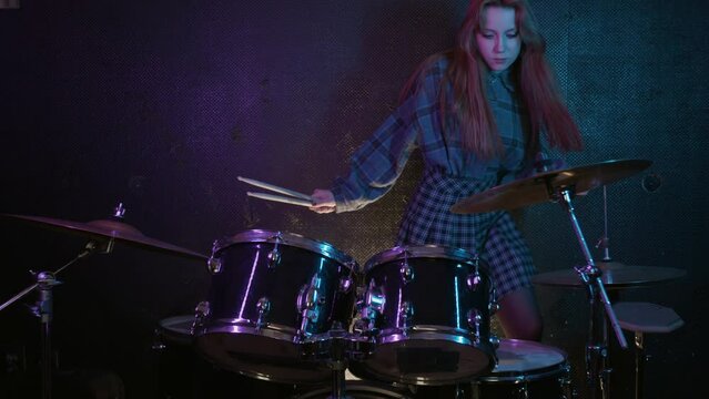 Cute young woman drummer sits down and starts to play the drums