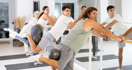 Sporty energetic males and females doing exercises with pilates ball during group training at gym. Fitness concept.