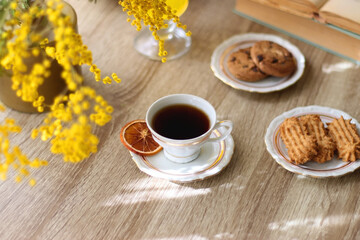 Cup of tea, plates with cookies, glass of orange juice, books, reading glasses, bowl of fruit and candles on the table. Selective focus.