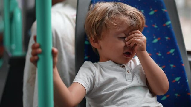 Tired Passenger boy sitting on bus seat holding on metal bar rubbing face and eyes wanting to sleep traveling