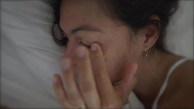 Woman rubbing eye laid in bed looking at phone. Tired sleepy female person rubs eye with finger