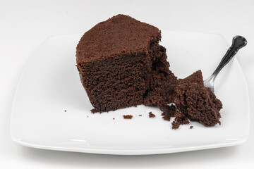 Textura porción de bizcocho de chocolate negro, casero, encima de un plato, aislado sobre fondo blanco. Serie