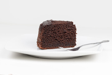 Porción de bizcocho de chocolate negro, casero, encima de un plato, aislado sobre fondo blanco....