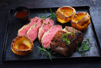 Traditional Commonwealth Sunday roast beef sliced with Yorkshire pudding and red wine sauce served...