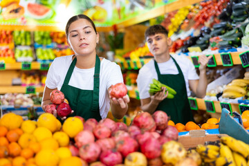 Confident young saleswoman working in a vegetable store puts pomegranates on the counter for sale