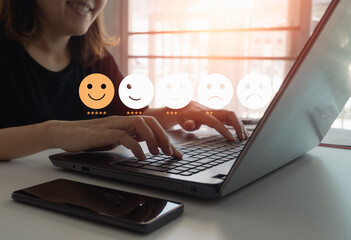 Young Asian happy woman using laptop computer and give a rating to service experience on online application for Customer review satisfaction feedback survey concept. Work from home.