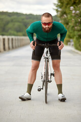 Young smiling sporty man in glasses with beard standing with bike in summer park, cardio workout on bike, city walks with bike, weight control