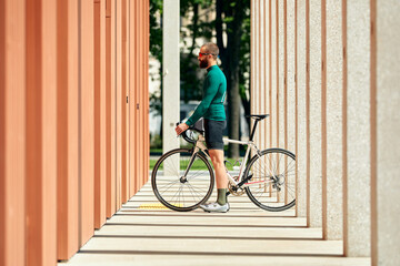 A professional cyclist in sportswear, a safety helmet and goggles is preparing for a morning bike ride in the urban concrete architecture. The concept of an active and healthy lifestyle.