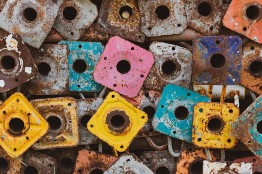 Old scaffold tubes are stored outside in a pile. Different colors yellow pink green tubes baseplates. Parts of the scaffolding. Scaffolding base vintage wallpaper. Standard workpiece scaffolds.