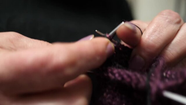 Close-up of the hands of an adult woman who knits socks with woolen threads using knitting needles.
