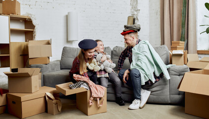 Playful funny parents and daughter. Young happy family, man, woman and kid moving into new flat, apartment with many cardboard boxes. Concept of moving houses, real estate, family, new life