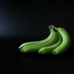 A bunch of fresh ripe green plantain bananas on a dark gradient background. Four bananas. Copy space © slexp880