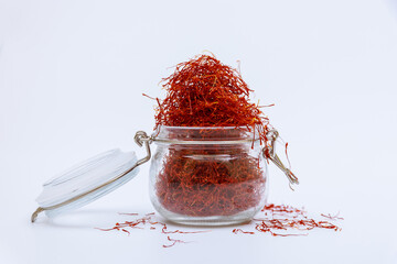 An overflowing glass jar of dry saffron stamens on a white table. Dry spice, use in cooking and...