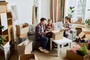 Fototapeta na wymiar Putting things on place. Young happy family, man, woman and kid moving into new flat, apartment with many cardboard boxes. Concept of moving houses, real estate, family, new life