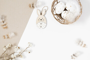 Easter holiday composition.Top view of Easter eggs in nest, feathers, rabbit, dry flowers, plants on light beige and white background. Minimal concept Easter. Flat lay, copy space