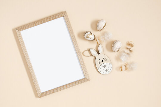 Easter trendy composition. Photo frame top view, feathers , easter eggs and bunny on beige background. Minimal concept Easter. Flat lay, top view, copy space