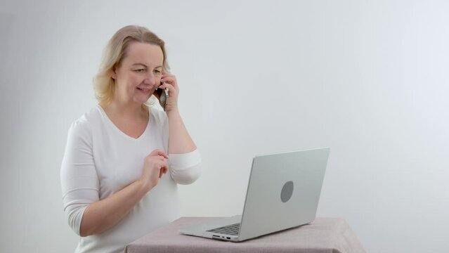 woman shares on the phone news that she saw on the Internet. She points with a finger at a laptop on a white background, smiles, talks with friends, telling interesting facts about the story