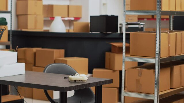 Empty storage room with office desk and shelves, warehouse filled with boxes of retail products. Order management and quality control space for stock merchandise, small business.