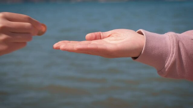 Female hand with coin by sea. A female give a coin to child against sea waves on beach.