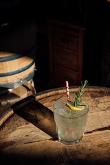 rosemary lemonade soda cocktail with ice and picnic gingham drinking straw on whiskey barrel happy hour