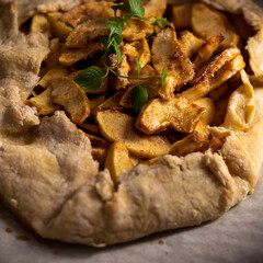 Rustic apple galette on parchment paper garnished with a sprig of mint.