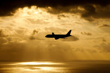 The plane flies over the sea in the sun rays.