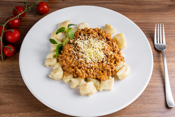 GNOCCHI COOKED WITH GROUND MEAT IN TOMATO SAUCE, COVERED IN GRATED CHEESE MOUNTED ON A WHITE PLATE ON A CHEERED TOWEL.
