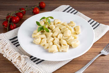 BAKED GNOCC IN A WHITE PLATE ON A WOODEN BACKGROUND. DETAIL OF BASIL AND SMALL TOMATOES.