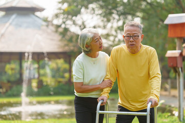 Elderly Asian couple and wife caring for their family enjoying retirement together in park. Old Caregiver people take close care while using walking cane stick.