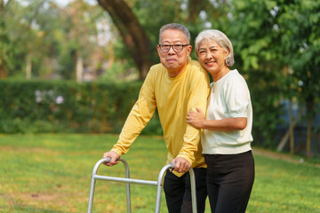 Elderly Asian couple and wife caring for their family enjoying retirement together in park. Old Caregiver people take close care while using walking cane stick.