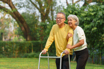 Elderly Asian couple and wife caring for their family enjoying retirement together in park. Old Caregiver people take close care while using walking cane stick.