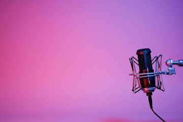a black microphone on black background under the neon light. podcasting, singing, and recording...